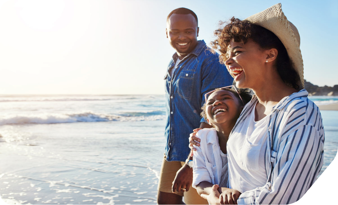 A husband and wife walk with their daughter on a sunny beach